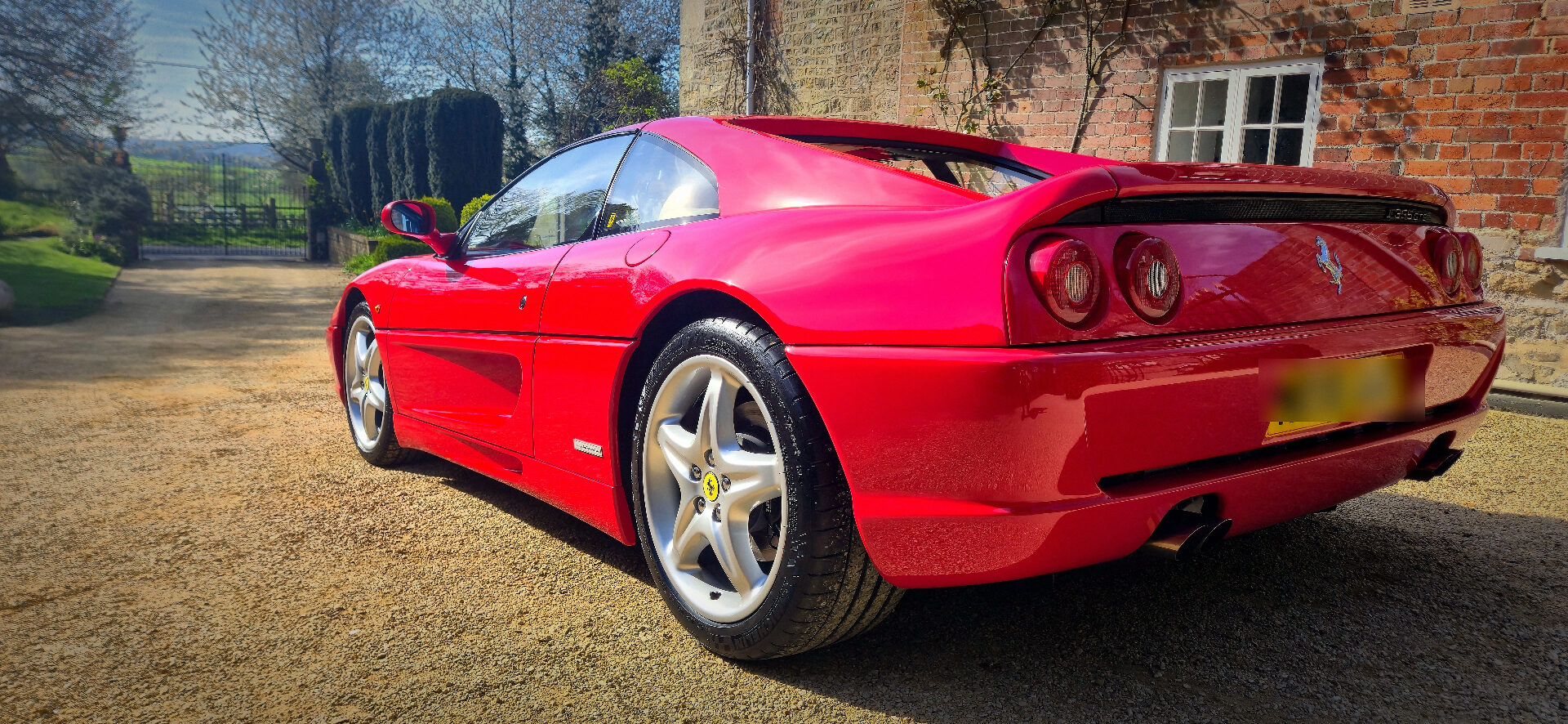 The creator's red Ferrari F355 GTS parked on a gravel driveway in the English countryside